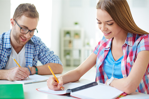 Two students writing down information whilst sitting at a college desk